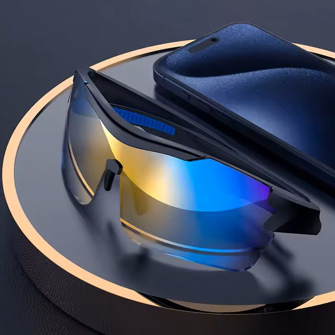 Sport sunglasses with a black frame and a reflective blue-to-yellow mirrored lens, displayed on a dark circular platform next to a smartphone case.