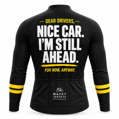 Black long-sleeve cycling jersey shown from the back with bold white and yellow text reading “DEAR DRIVERS, NICE CAR. I’M STILL AHEAD.